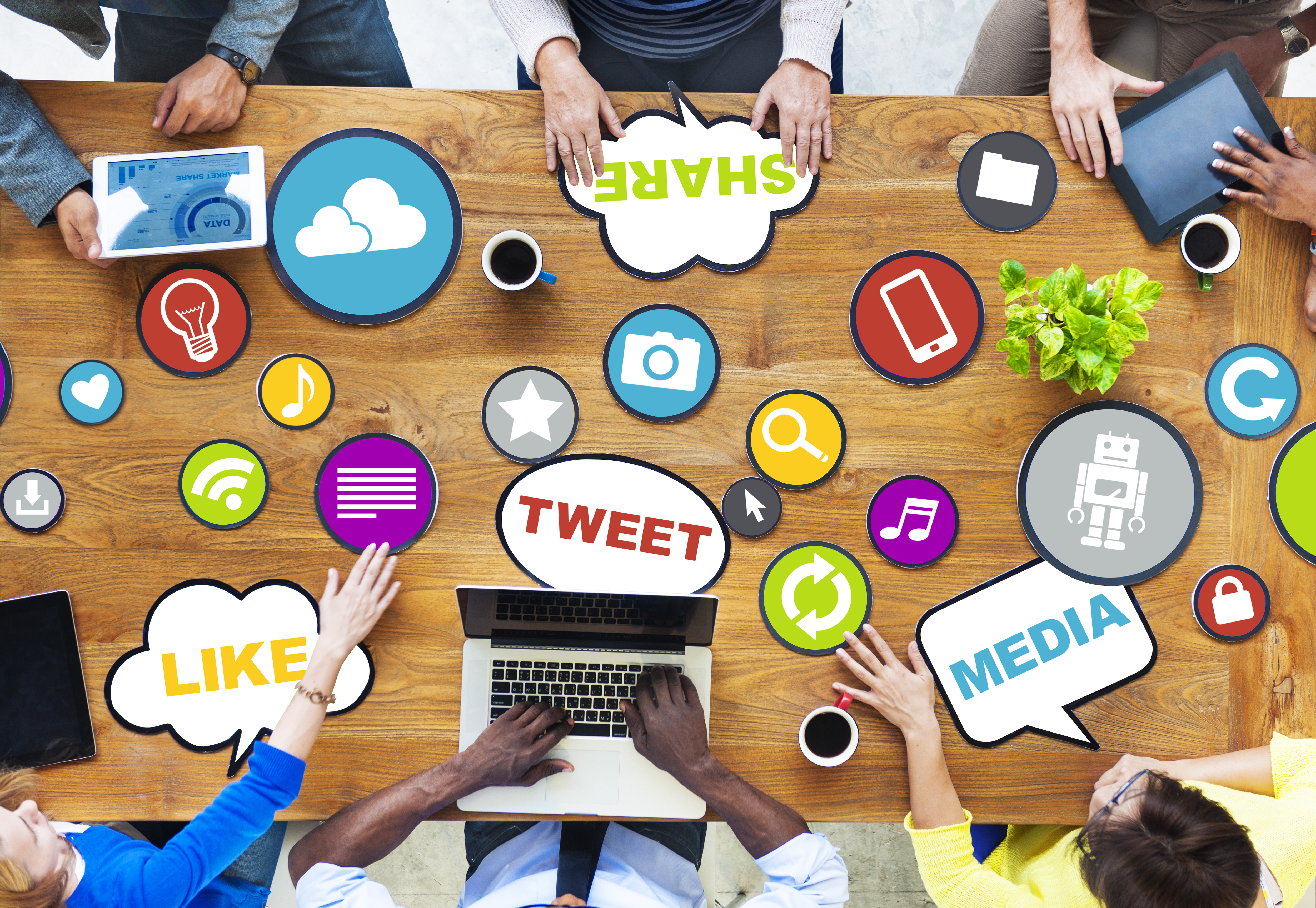 Technological symbols on a table with a team collaborating about social media marketing